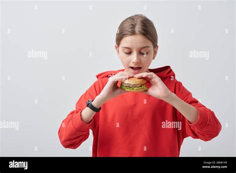 Youthful Girl In Red Hoodie Holding Appetizing Hamburger By Her Open