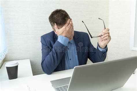 Tired Or Exhausted Man Closing His Face With Hands Sitting In Front Of