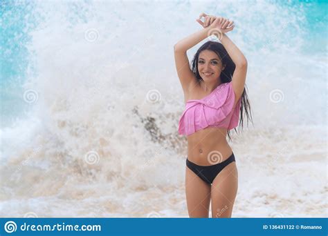 Tanned Girl In Swimsuit With Raised Arms Posing On Beach Near Ocean