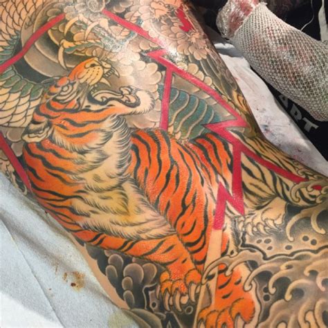 A Man With A Large Tiger Tattoo On His Back And Arm Sitting In A Chair
