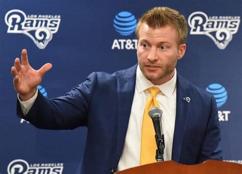 A Man In A Suit And Tie Speaking Into A Microphone At A Rams Press