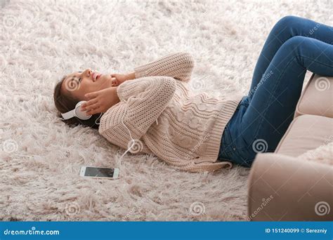 Beautiful Young Woman Listening To Music While Lying On Carpet At Home