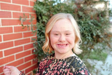 Happy Teen Girl With Down Syndrome Smiling By Brick Wall On Sunny Day