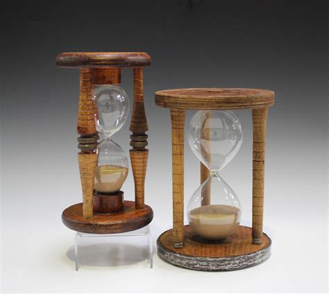 two 20th century sand timer hourglasses mounted within wooden frames heights 24cm and 25cm