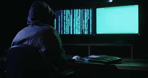 Anonymous Hacker Sitting In A Dark Room In Front Of Screens And Hacking