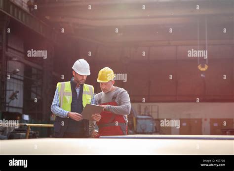 Male Foreman And Worker With Clipboard Talking In Factory Stock Photo