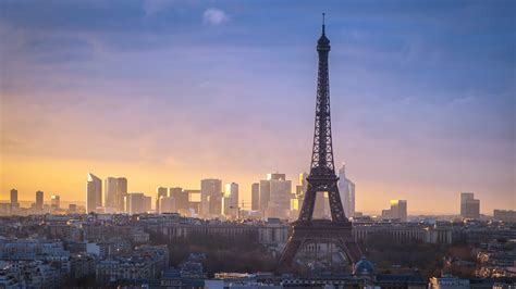 Paris Eiffel Tower With Background Of Taller Buildings And Cloudy Sky