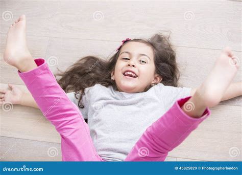High Angle View Of Playful Girl Lying On Floor With Legs Raised At Home Stock Image Image Of