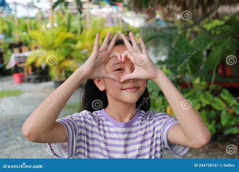 Portrait Of Asian Girl Doing Heart Shape With Hand And Fingers Smiling Looking Through Sign In