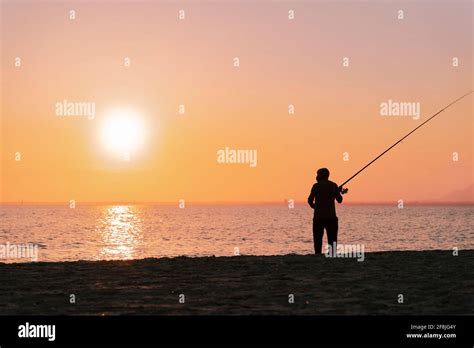 Silhouette Of Man Fishing In Waves On Beach At Sunset Stock Photo Alamy