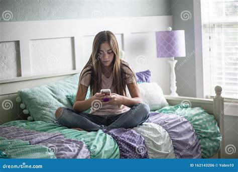 Adolescent Teen Girl Texting On A Smartphone Sitting In Bed At Home In