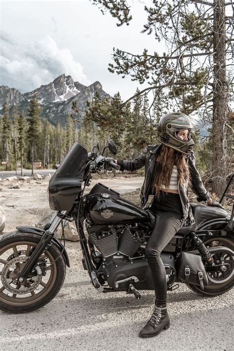 A Woman Sitting On Top Of A Motorcycle Next To A Forest Filled With