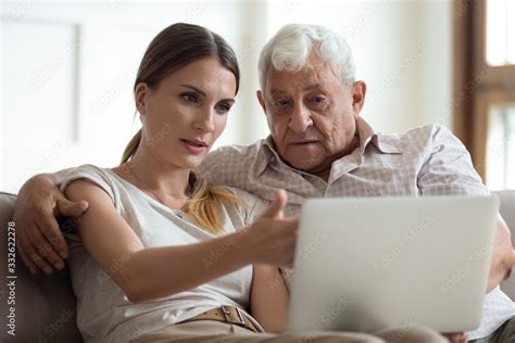 serious adult daughter helping older father with laptop close up pointing at screen explaining