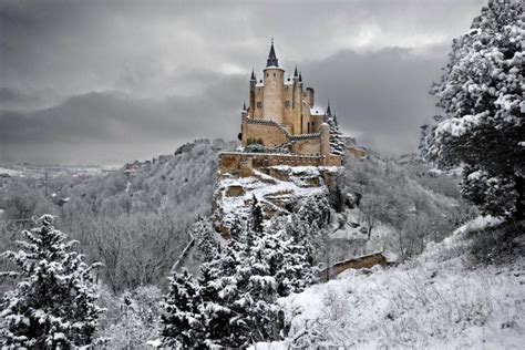 A Castle On Top Of A Snowy Hill With Trees In The Foreground And Dark