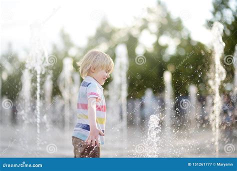 Little Boy Plays In The Square Between The Water Jets In The Fountain