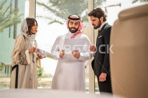 رجل اعمال عربي سعودي خليجي بالثوب السعودي التقليدي يتناقش مع عميل يرتدي البدلة الرسمية، اتفاقية