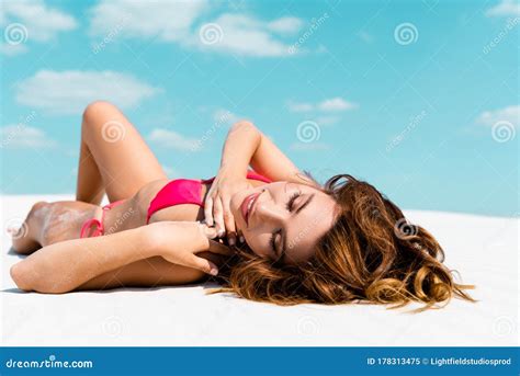 beautiful girl in swimsuit lying on sandy beach with blue sky and clouds at background stock