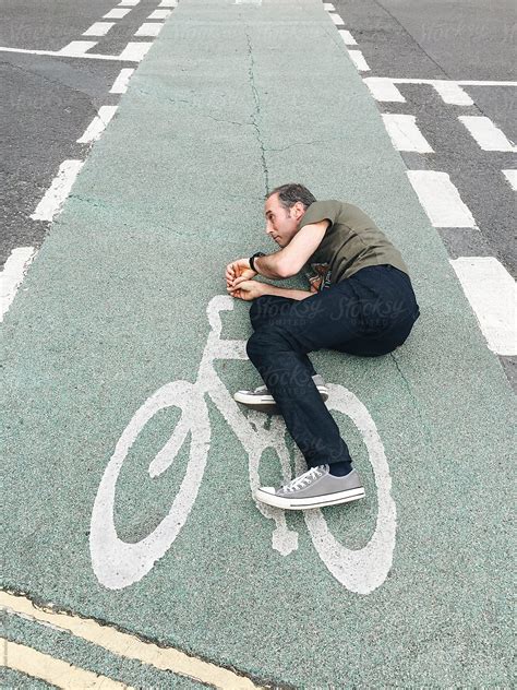 Man Lying On Tarmac Pretending To Ride A Bicycle That Is Painted On The Road Del Colaborador
