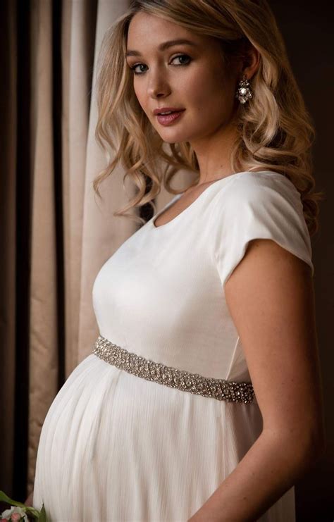 A Pregnant Woman In A White Dress Holding A Bouquet