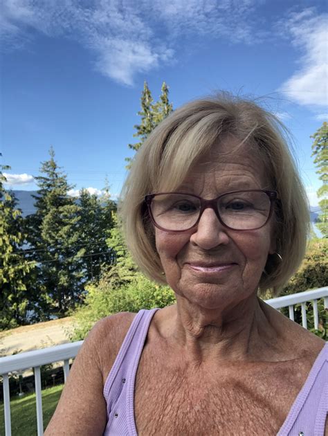 an older woman with glasses is smiling for the camera while sitting on a porch railing