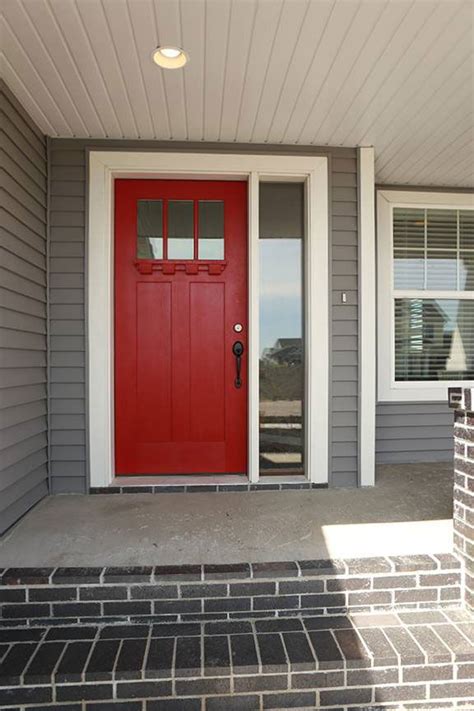 A Red Front Door With Two Windows And Brick Steps Leading To The