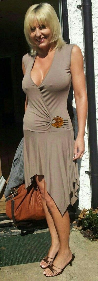 A Woman With Blonde Hair Wearing A Tan Dress And Holding A Brown Purse