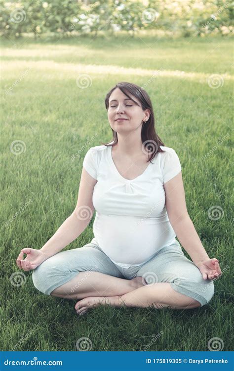 Young Pregnant Woman Meditating While Sitting In Lotus Position Stock