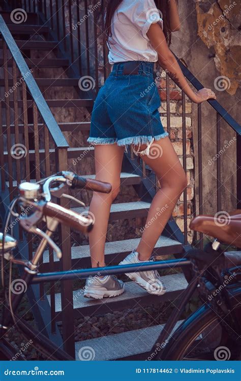 cropped image of a slim girl wearing short denim shorts and a white t shirt posing on stairs