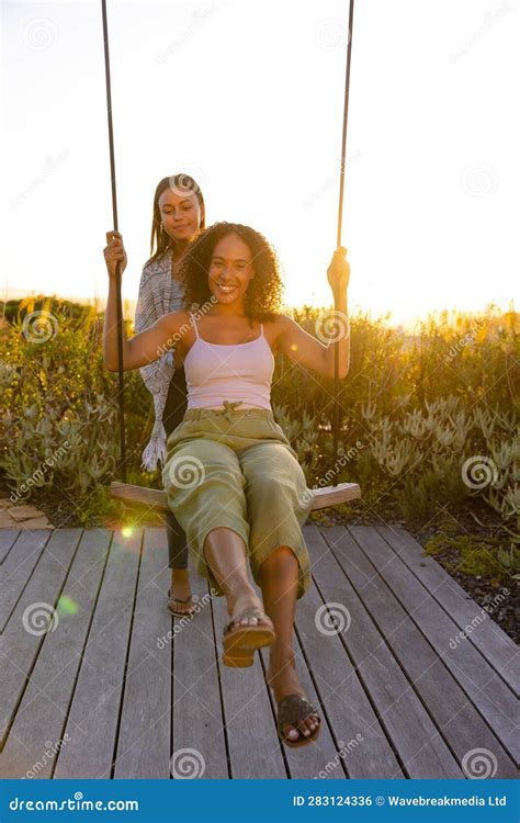 Happy Biracial Lesbian Couple Swinging On Swing In Sunny Garden Stock