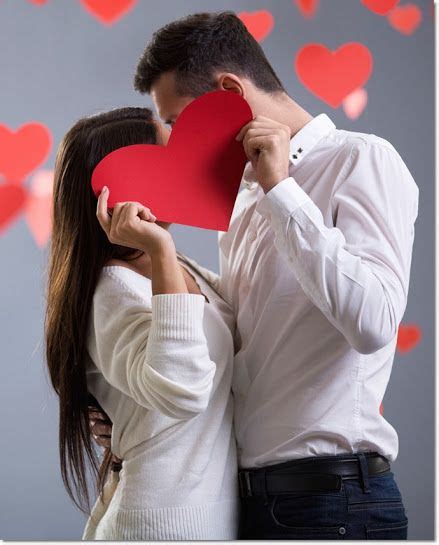 a man and woman holding up a red paper heart to their face with hearts flying in the background