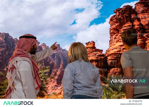 صورة مقربة من الخلف لزائرين اجانب مع مرشد سياحي سعودي يقف في منطقة العلا في السعودية و الاشارة