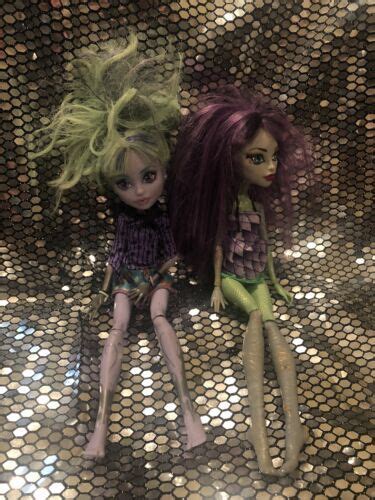 Two Dolls Sitting Next To Each Other On Top Of A Shiny Surface With Sequins