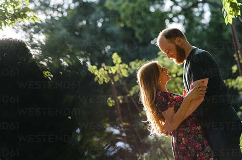 Smiling Heterosexual Couple Embracing While Standing In Park Stock Photo