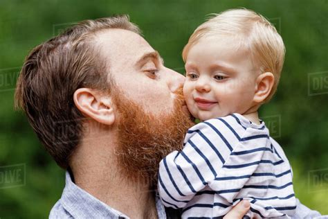 Portrait Of Father Kissing Baby Girl Outdoors Smiling Stock Photo