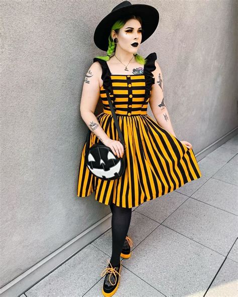 A Woman With Green Hair Wearing A Black And Yellow Striped Dress Holding A Cat Purse