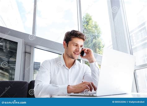 Happy Young Businessman Talking On Cell Phone And Using Laptop Stock