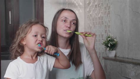 Mom And Her Cute Little Daughter Is Brushing Teeth With Toothbrushes
