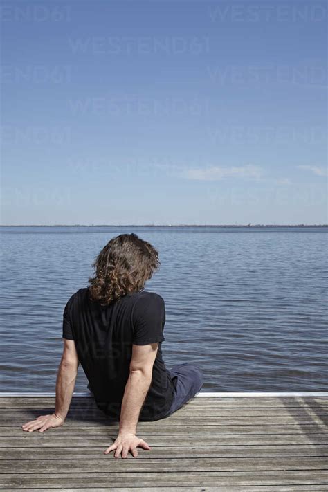Back View Of Man Sitting On Jetty Stock Photo