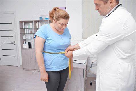 Male Doctor Measuring Waist Of Overweight Woman In Hospital Stock