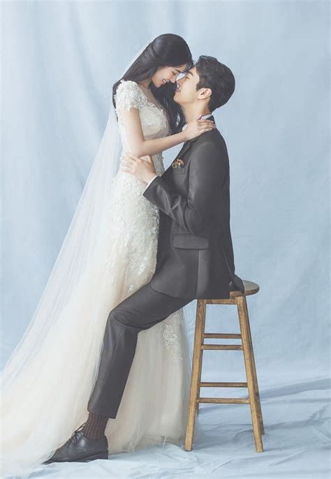 A Bride And Groom Are Sitting On A Stool Kissing Each Other In Front Of A White Backdrop