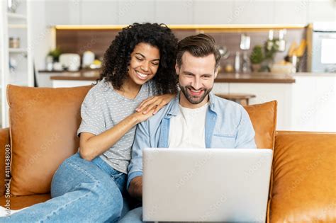 Multi Ethnic Couple In Love Spends Leisure Time With A Laptop At Home Multiracial Girlfriend