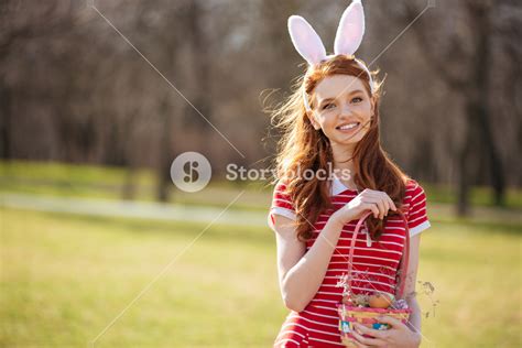 portrait of a joyful redhead girl with bunny ears and easter egg basket outdoors royalty free