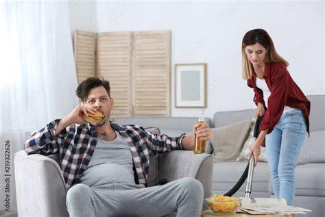 lazy husband watching tv and his wife cleaning at home stock foto adobe stock