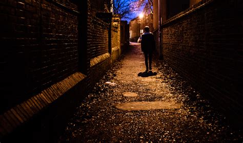 A Young Man Walking Home Alone At Night Through A Dark Alleyway In The