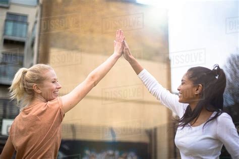 Two Young Women Giving High Five Outdoors Stock Photo Dissolve