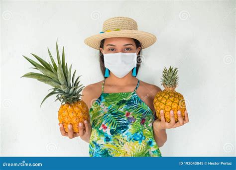 A Woman With A Mask And Straw Hat Holding Whole Pineapples Looking Into The Camera Stock Image