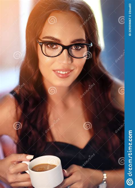 A Beautiful Caucasian Brunette With Glasses Is Sitting Inside The Room Holding A Cup Of Coffee