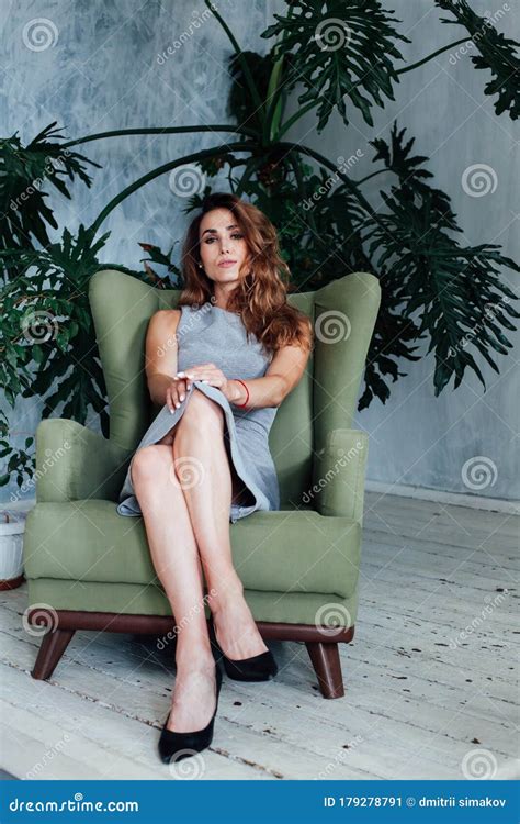 Portrait Of A Beautiful Fashionable Woman In A Gray Dress Sitting In A