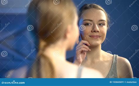 pretty girl touching facial skin near mirror satisfied with reflection beauty stock image