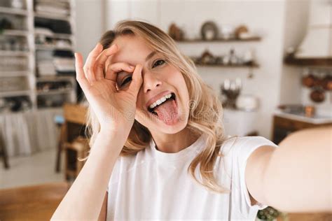 Image Closeup Of Amusing Blond Woman Looking At Camera And Taking Selfie Photo In Living Room